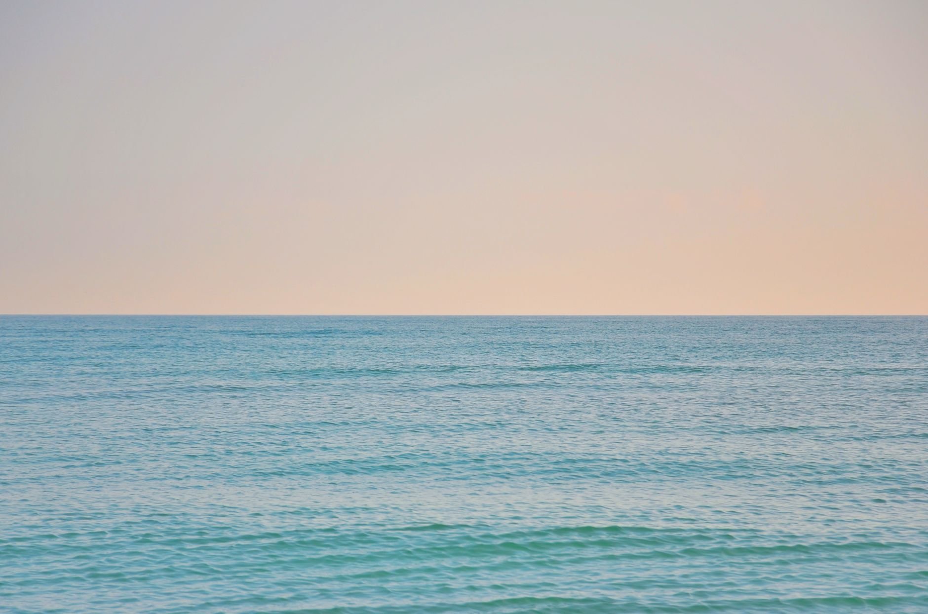 Calm blue ocean meeting subtle pastel sky, creating a peaceful horizon scene.